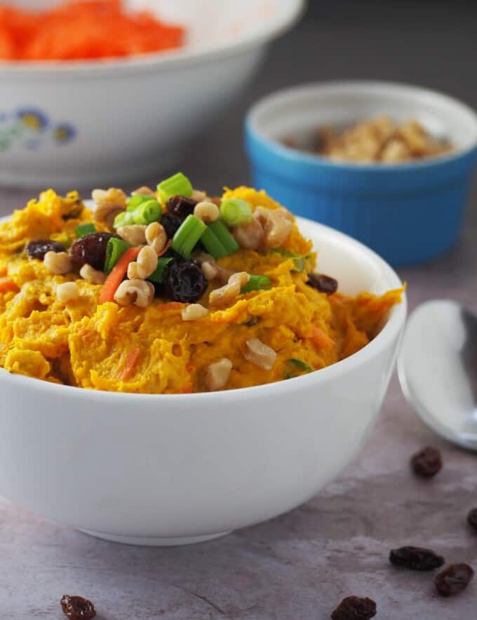 Kabocha Salad in a white bowl with bowls of shredded carrots and peanuts on the side