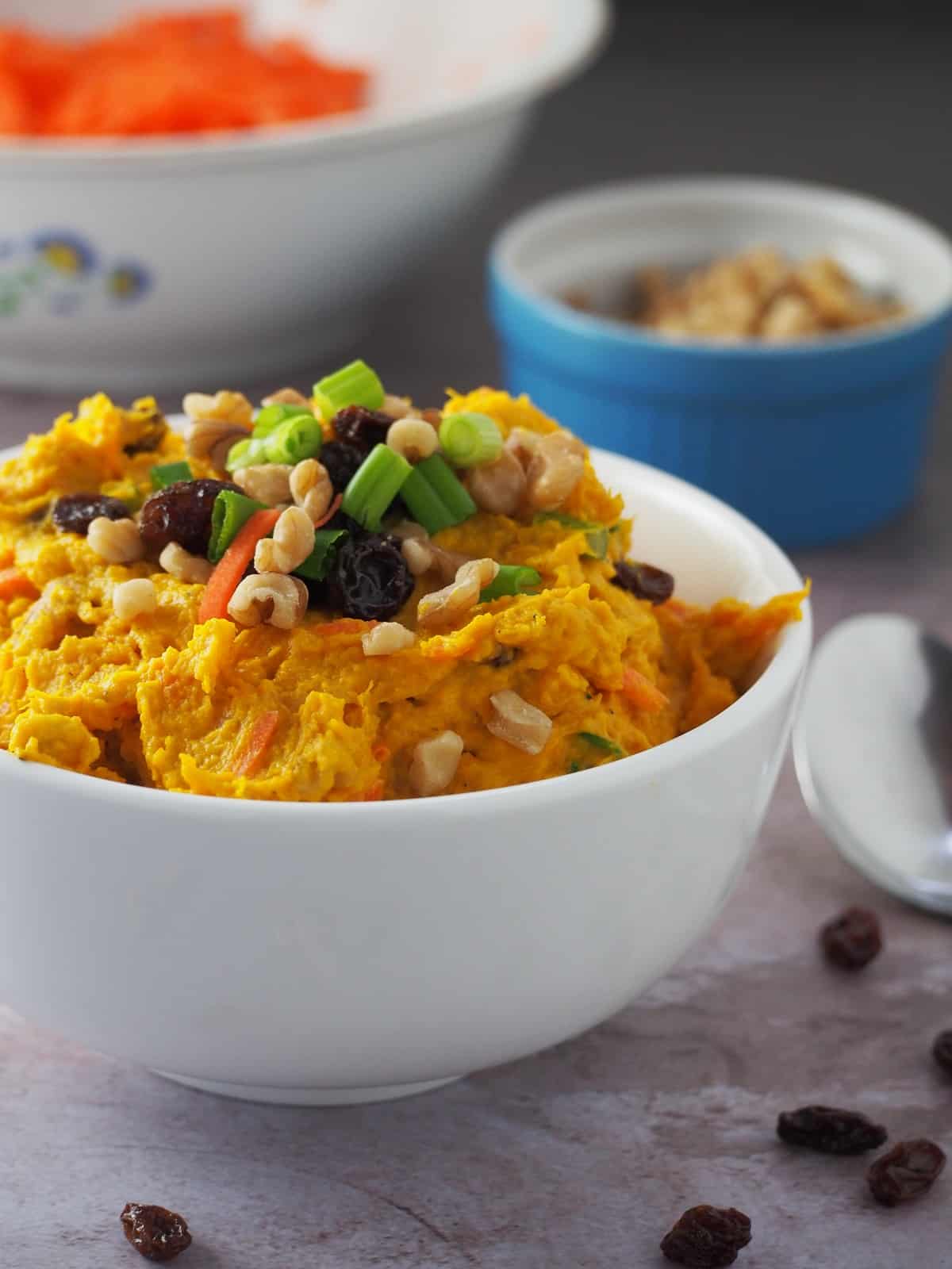 Kabocha Salad in a white bowl with bowls of shredded carrots and peanuts on the side