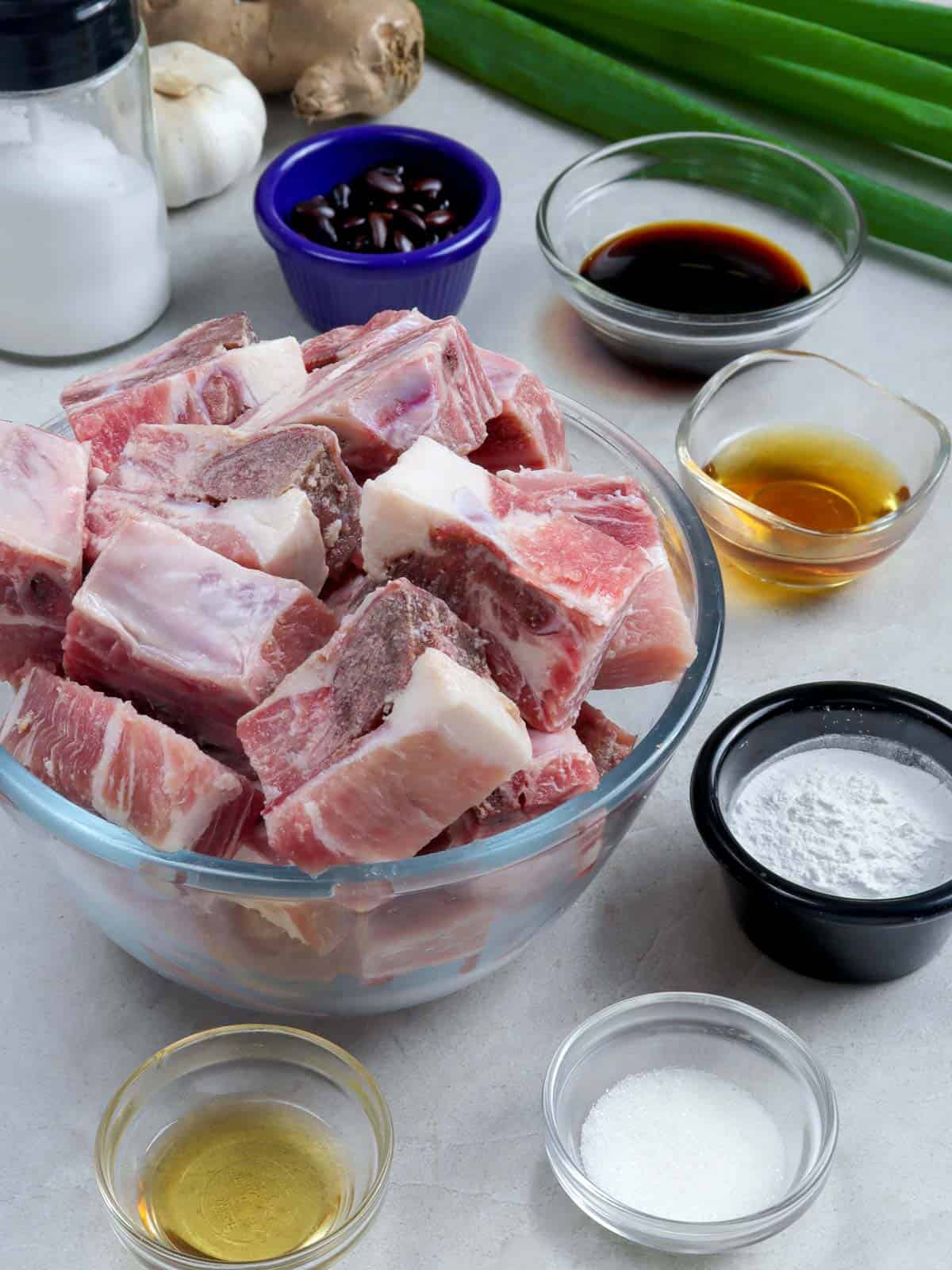 cut spare ribs in a bowl with black beans, soy sauce, and green onions on the side