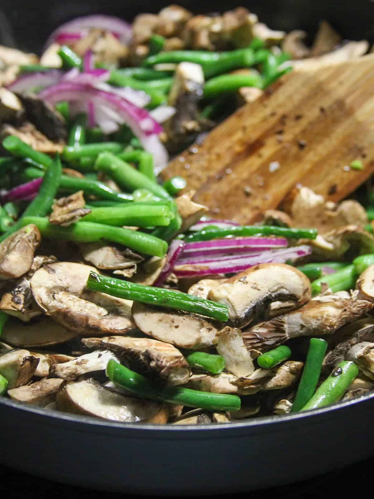 stir-frying green beans and sliced mushrooms in a wide pan