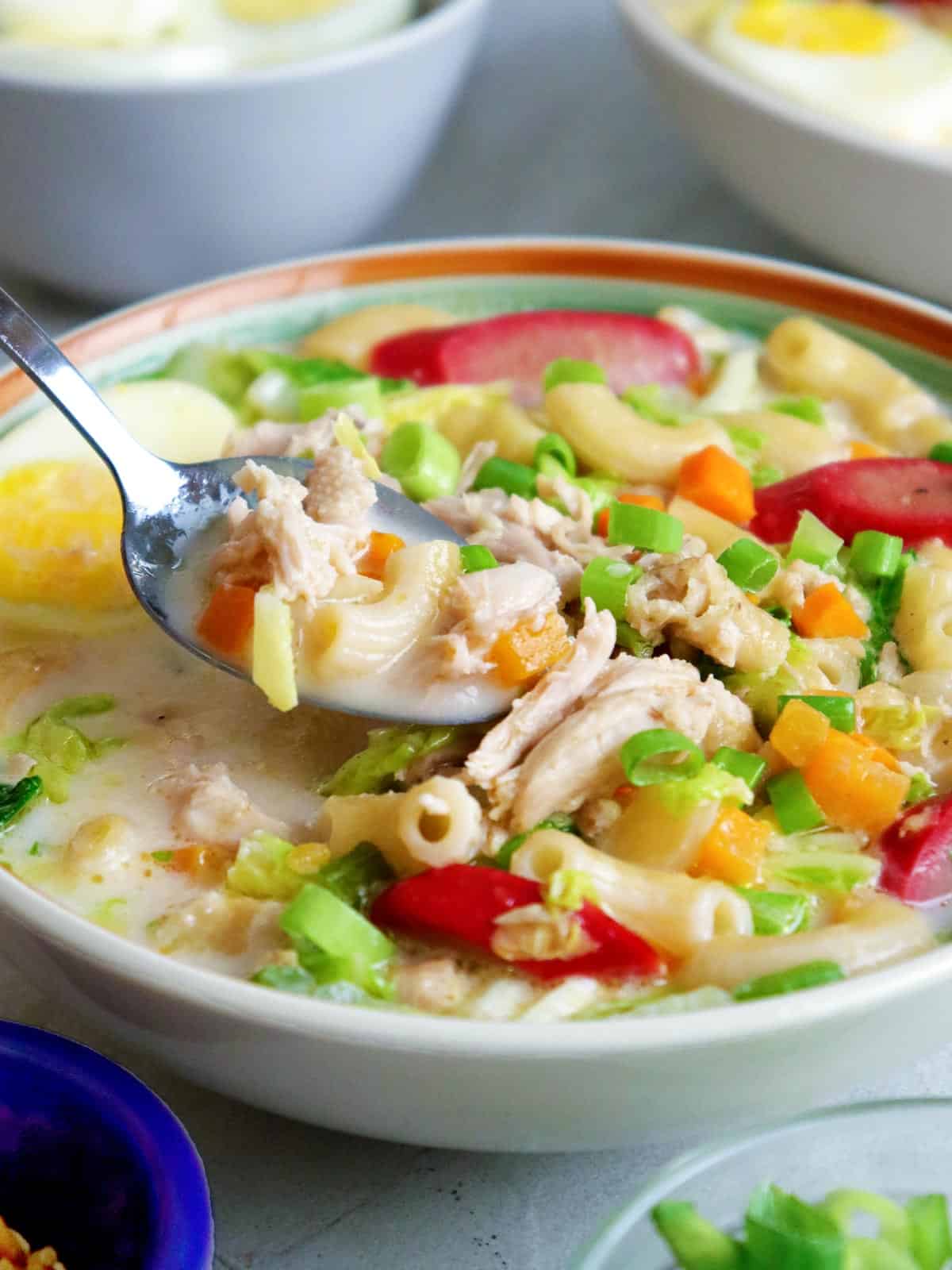 eating Filipino chicken macaroni soup with a spoon from a bowl