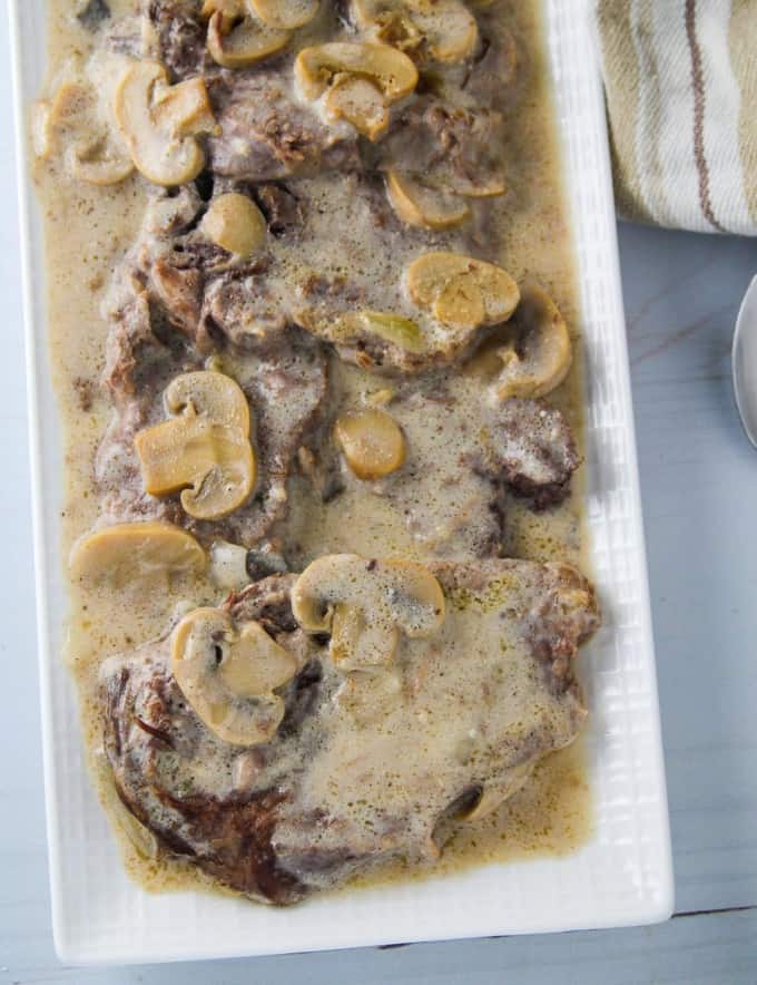 creamy lengua in mushroom gravy on a white serving platter