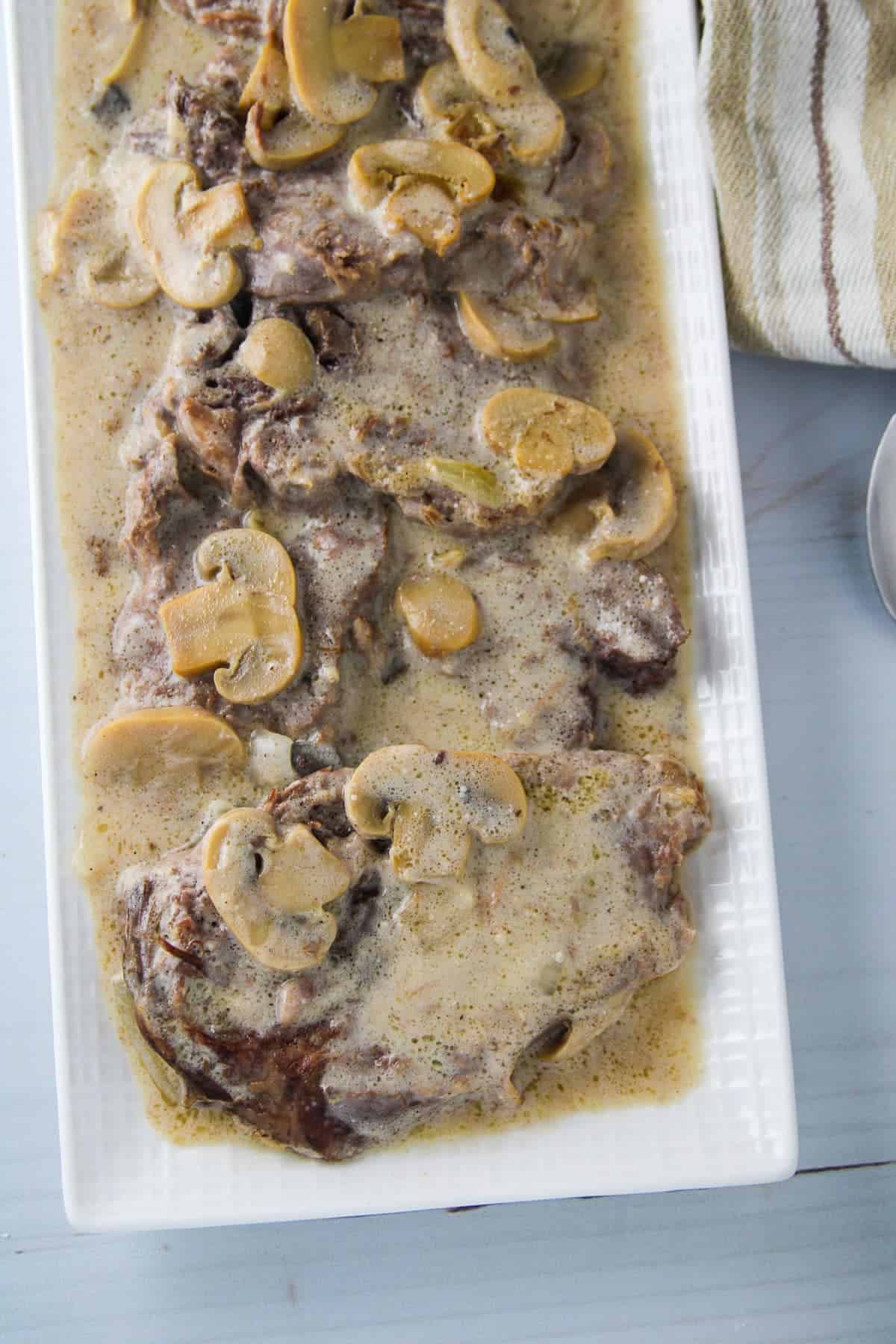 ox tongue with creamy mushroom gravy on a white serving platter