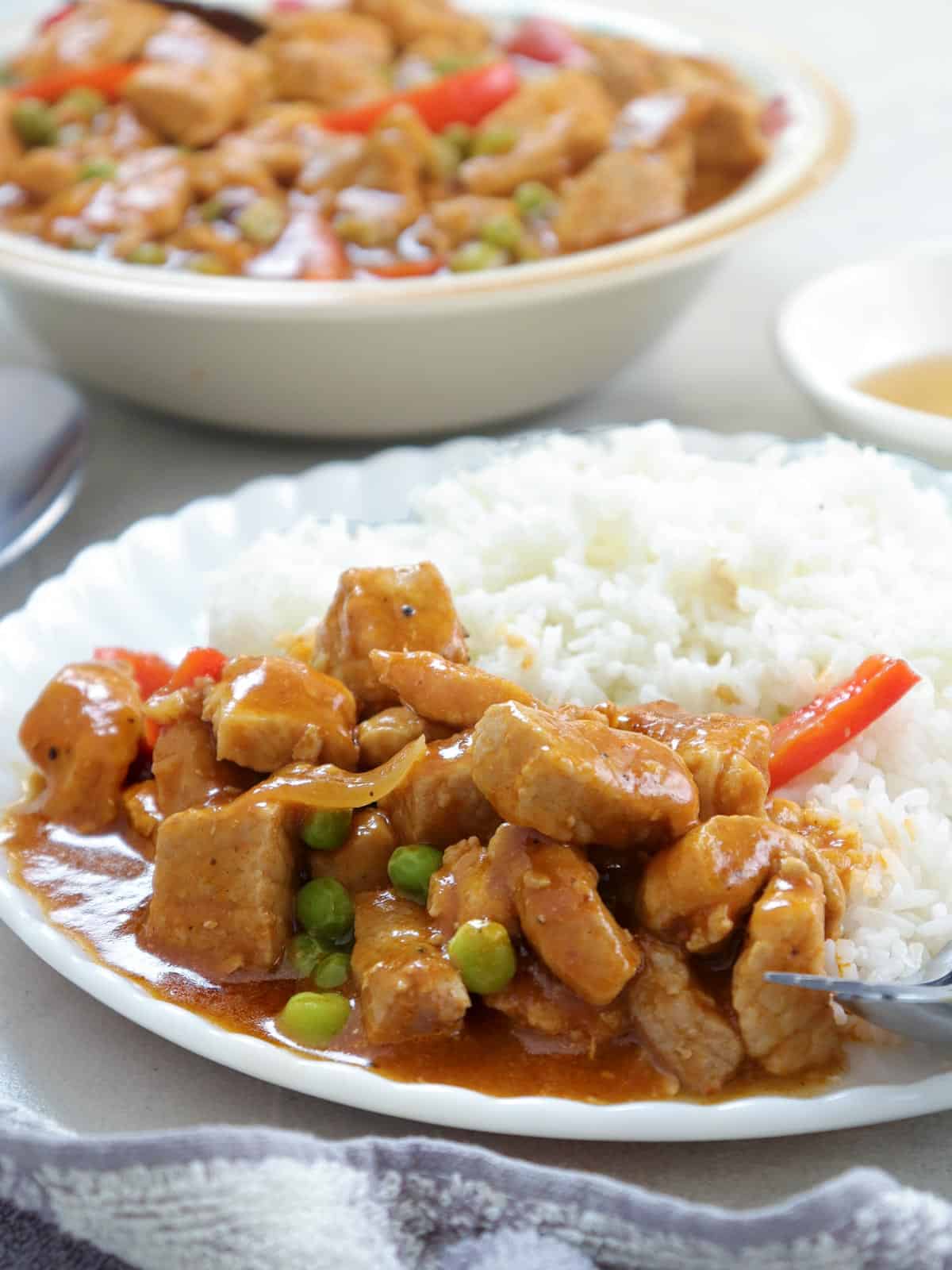 Filipino pork and peas stew on a white plate with steamed rice