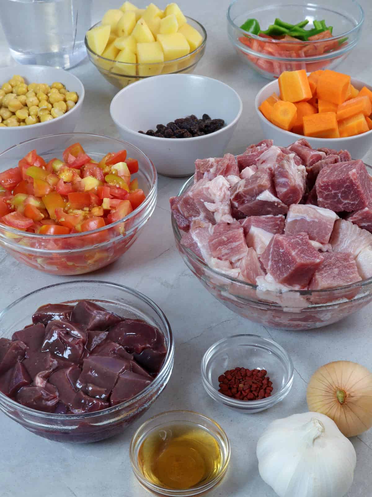 diced pork, sliced liver, fish sauce, oil, chopped tomatoes, diced carrots, onion, garlic, dicedpotatoes, garbanzo beans, raisins in individual bowls