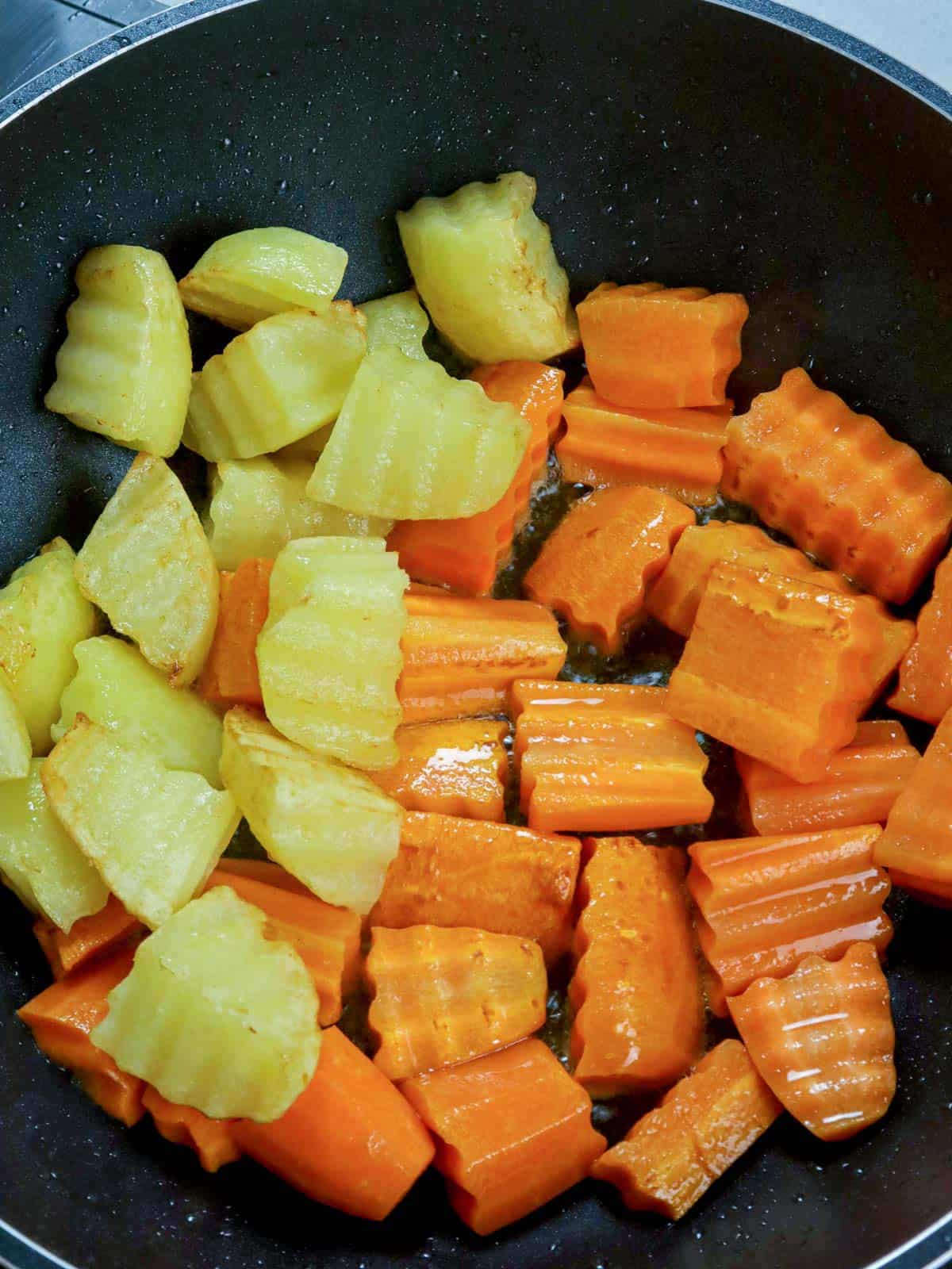 pan-frying cubed potatoes and carrots in a pan