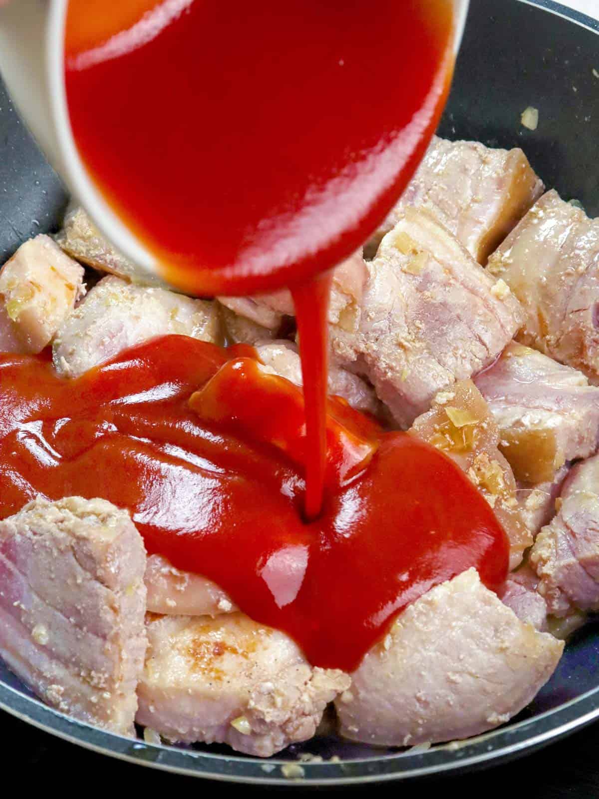 pouring tomato sauce over browned pork belly in a pan