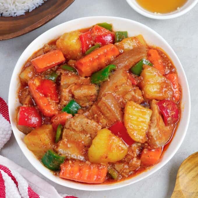 afritadang baboy with carrots, potatoes, and bell peppers in a white serving bowl