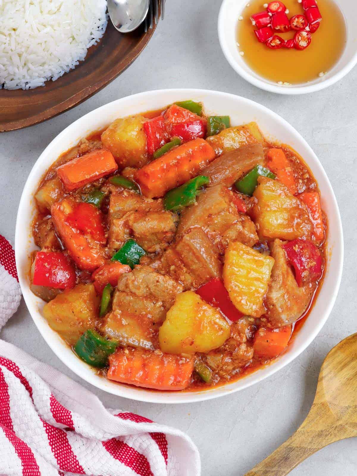 afritadang baboy with carrots, potatoes, and bell peppers in a white serving bowl