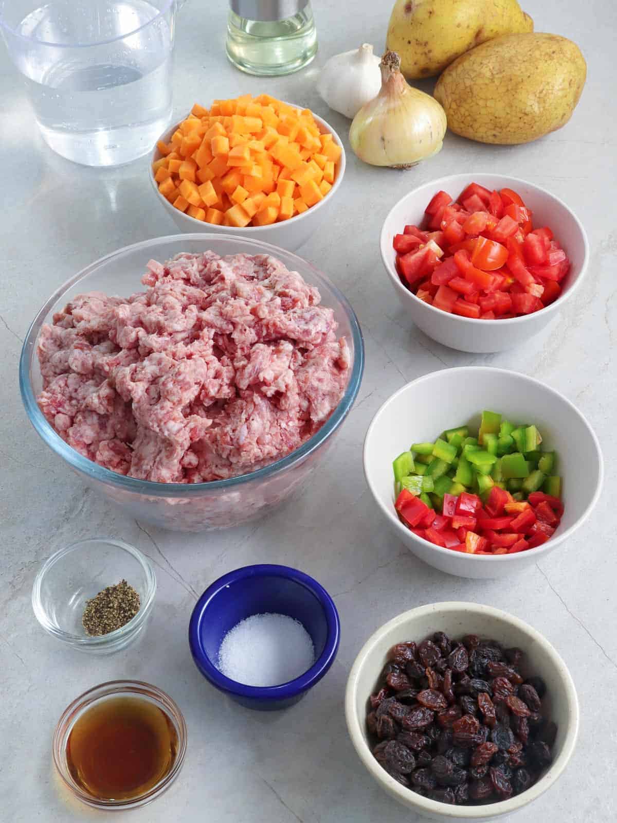 ground pork, diced bell peppers, chopped fresh tomatoes, diced carrots, potatoes, salt, peppers, raisins in individual bowls