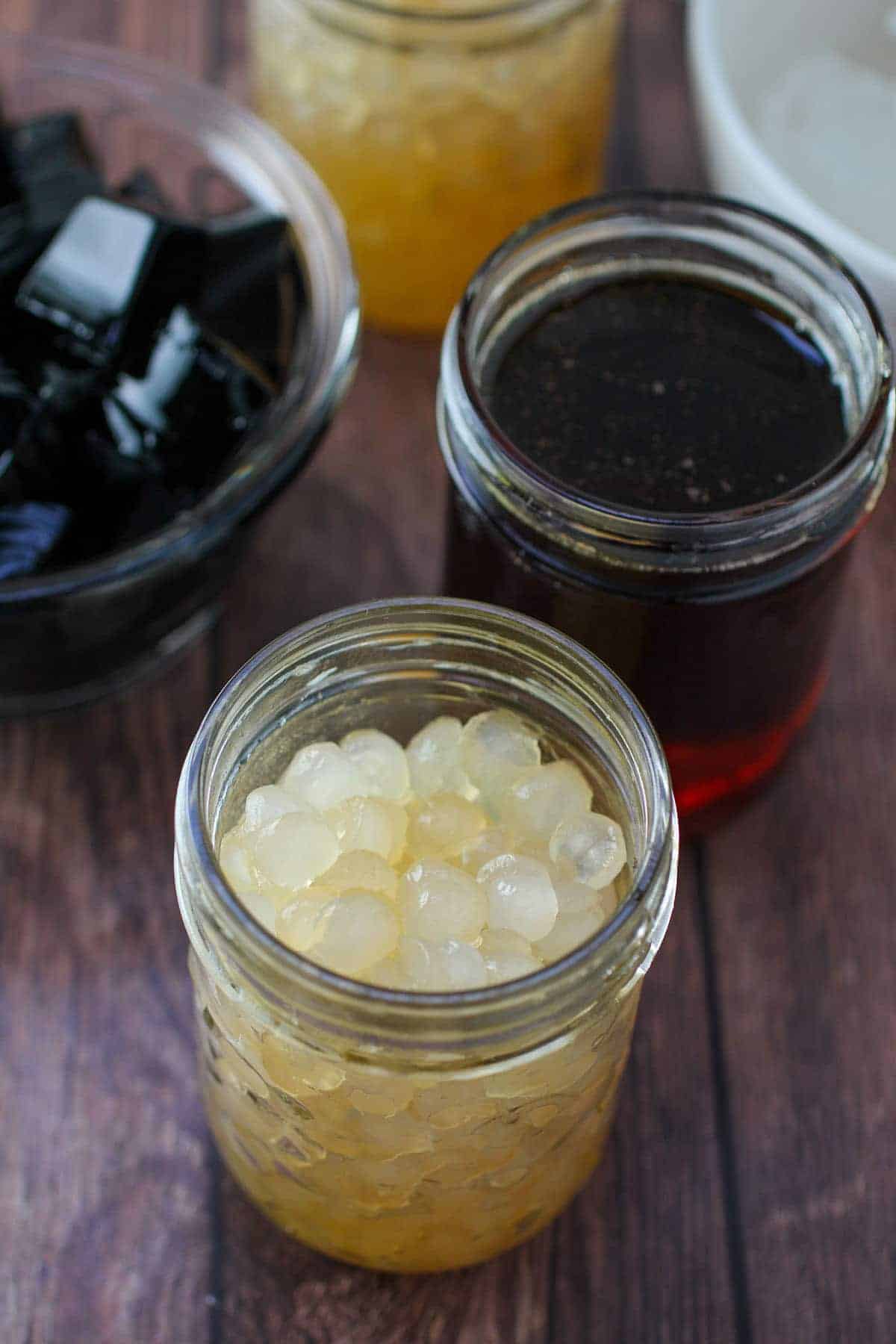 cooked sago and arnibal syrup in jars and black jelly cubes in a bowl