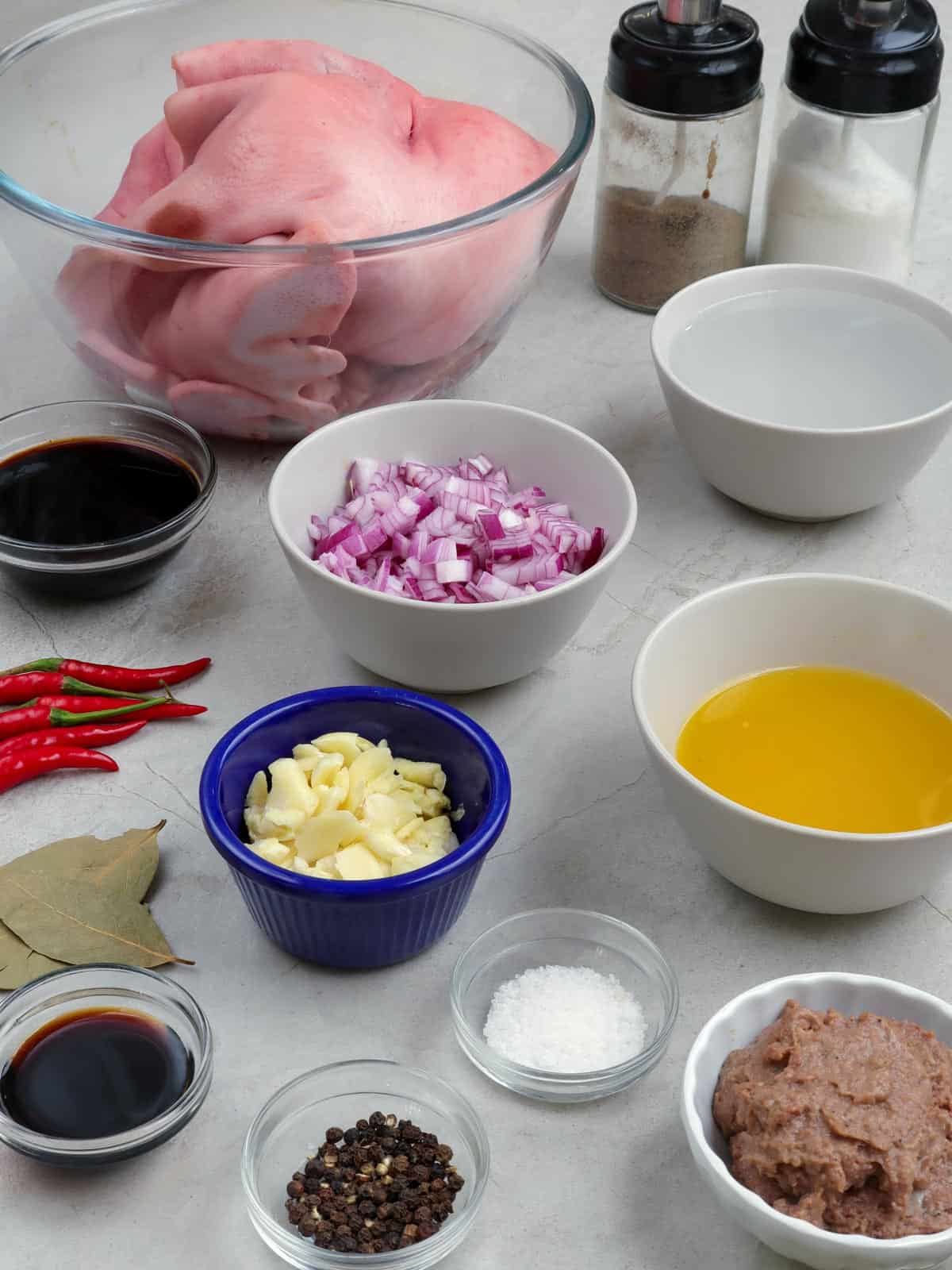 pork face, calamansi juice, chopped onions, garlic, liver spread, chili peppers, peppercorns, salt, soy sauce, bay leaves in bowls