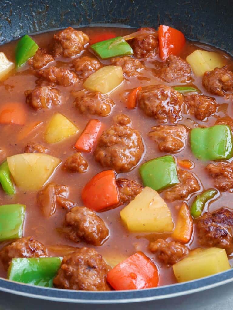sweet sour meatballs with bell peppers and pineapple chunks in a pan