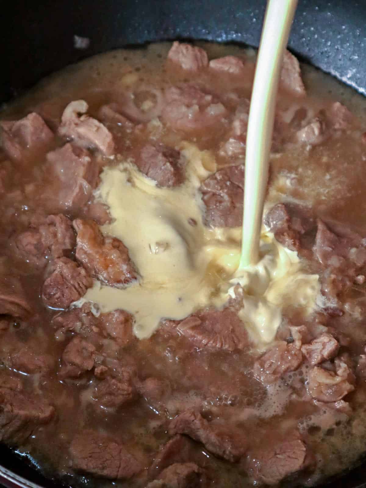 pouring cream to a pan of pork stew