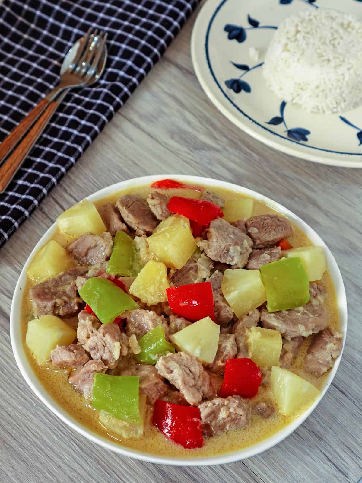 Pininyahang Baboy in a serving bowl with a plate of steamed rice on the side