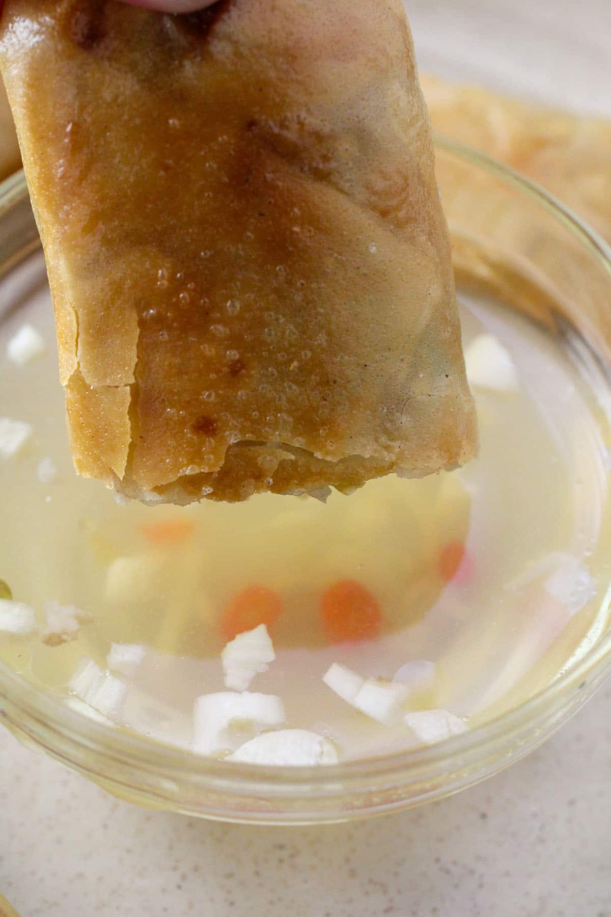 dipping fried lumpia in a bowl of spicy vinegar