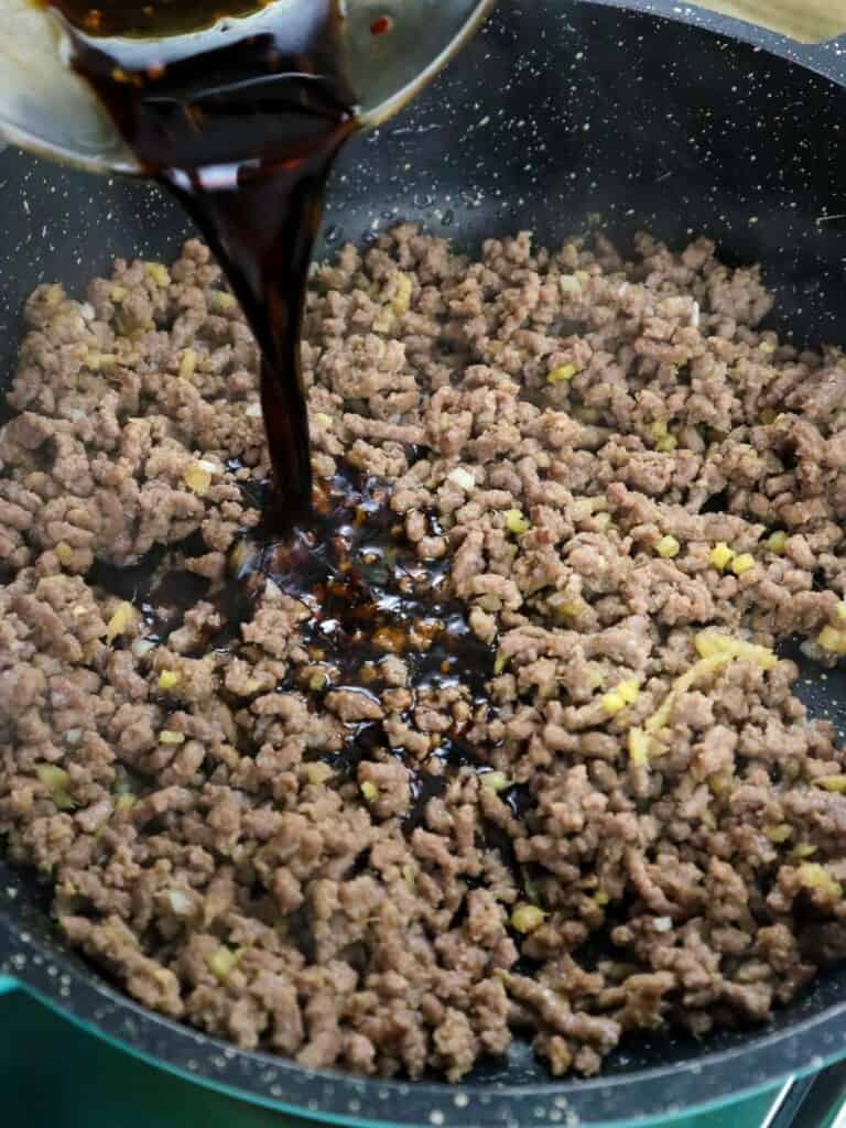adding sauce to browned ground beef in a pan