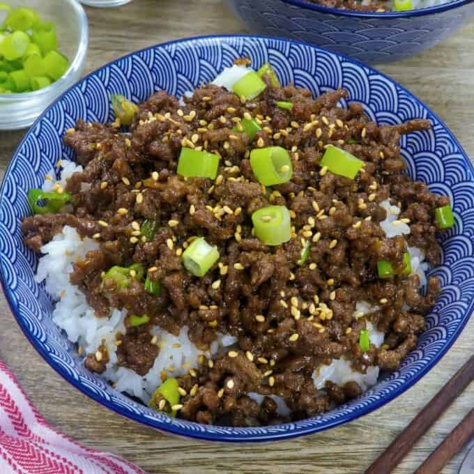 Korean Ground Beef on a bed of steamed rice garnished with green onions and sesame seeds in white serving bowl