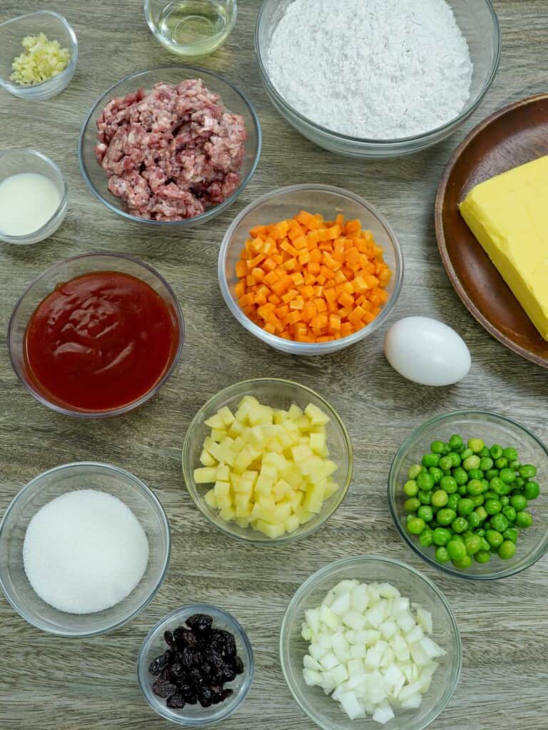 ground beef, tomato sauce, green peas, diced potatoes, diced carrots, flour, butter, salt, sugar, flour, onions, garlic, egg, oil in bowls