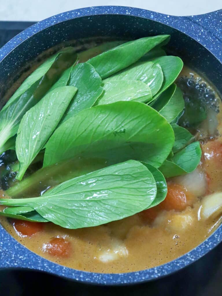 adding bok choy to a pot of sinigang soup