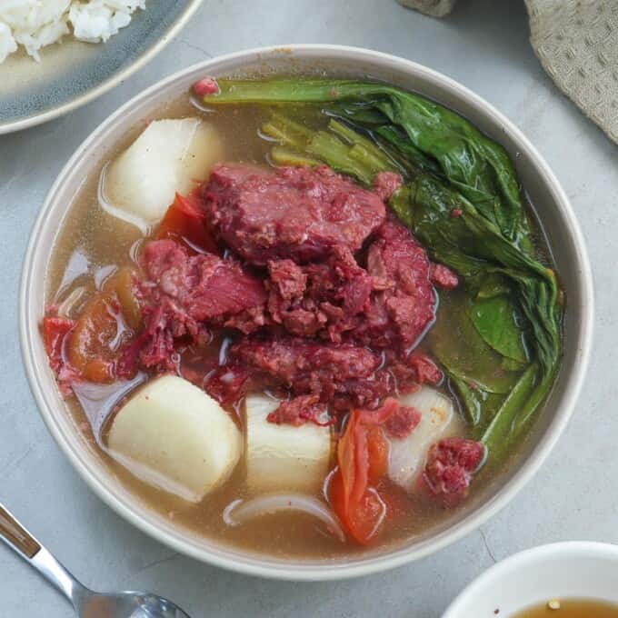 sinigang na corned beef in a white bowl with a plate of rice on the side