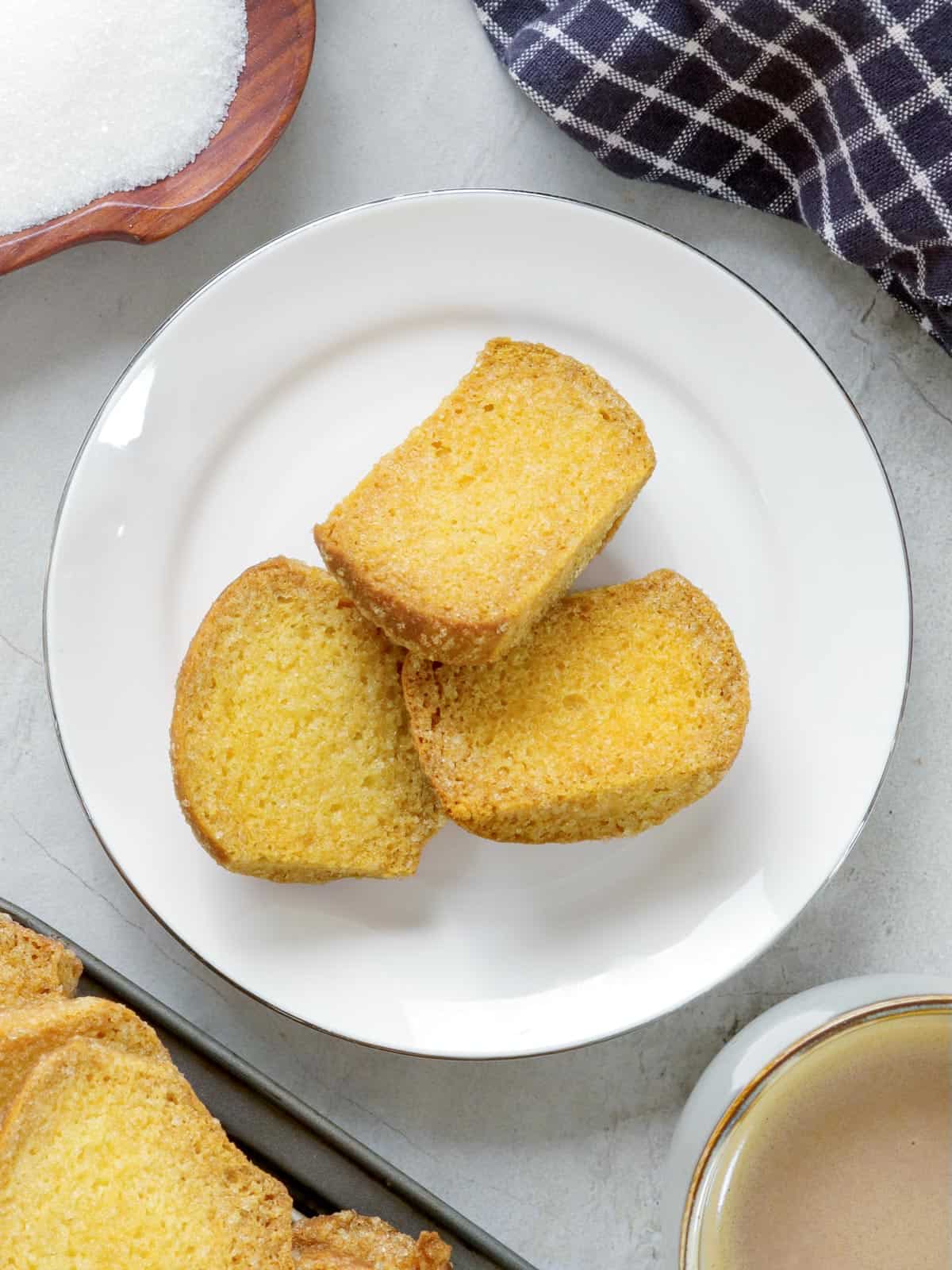 homemade biscocho on a white plate with mugs of coffee on the side