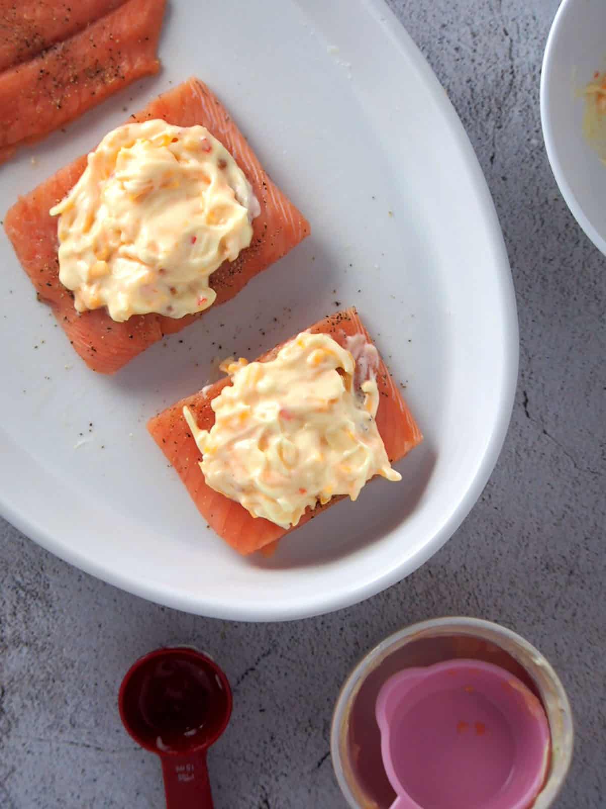 raw salmon fillets topped with sweet chili sauce, mayonnaise and cheese mixture on a white plate