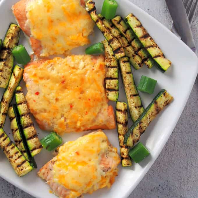 salmon with cheesy sweet chili mayo topping on a plate with grilled zucchini