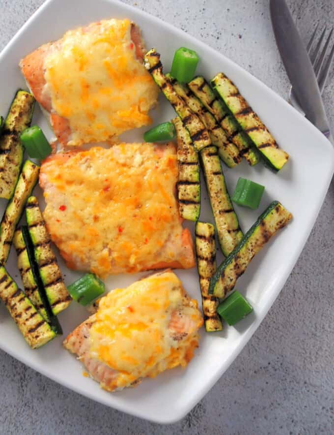 salmon with cheesy sweet chili mayo topping on a plate with grilled zucchini