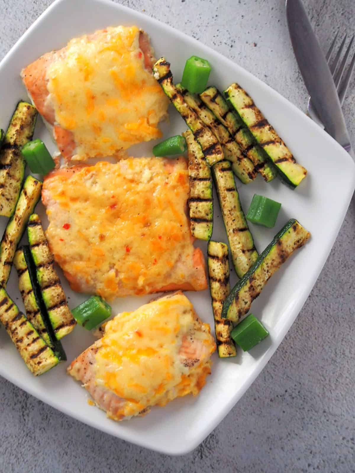 salmon with cheesy sweet chili mayo topping on a plate with grilled zucchini