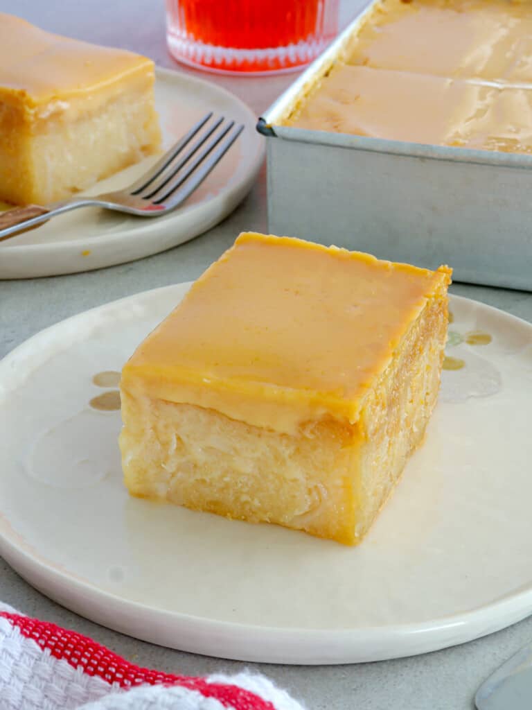 slice of cassava cake with custard topping on white serving plate.