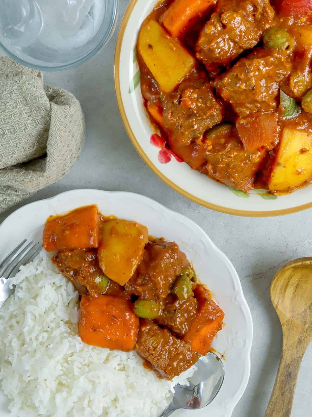 Beef Caldereta with white rice on a white plate with spoon and fork