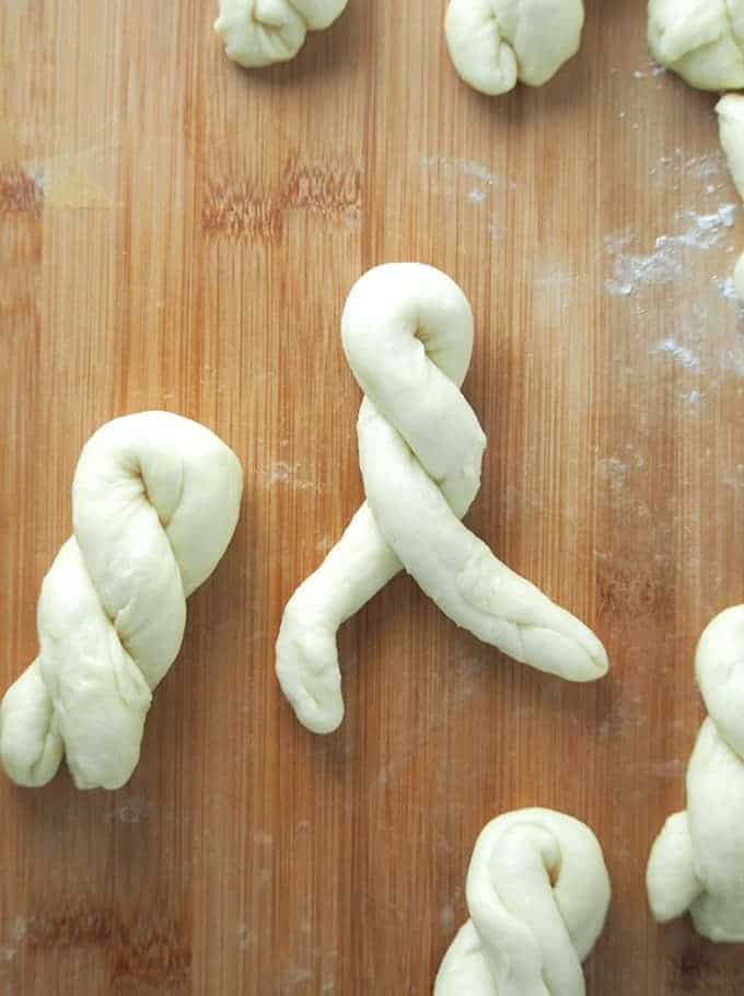 shaping yeast dough into twisted ropes on a wooden board to make bitso-bitso 