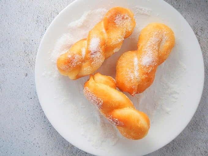 coating fried shakoy donuts with sugar in a shallow white plate