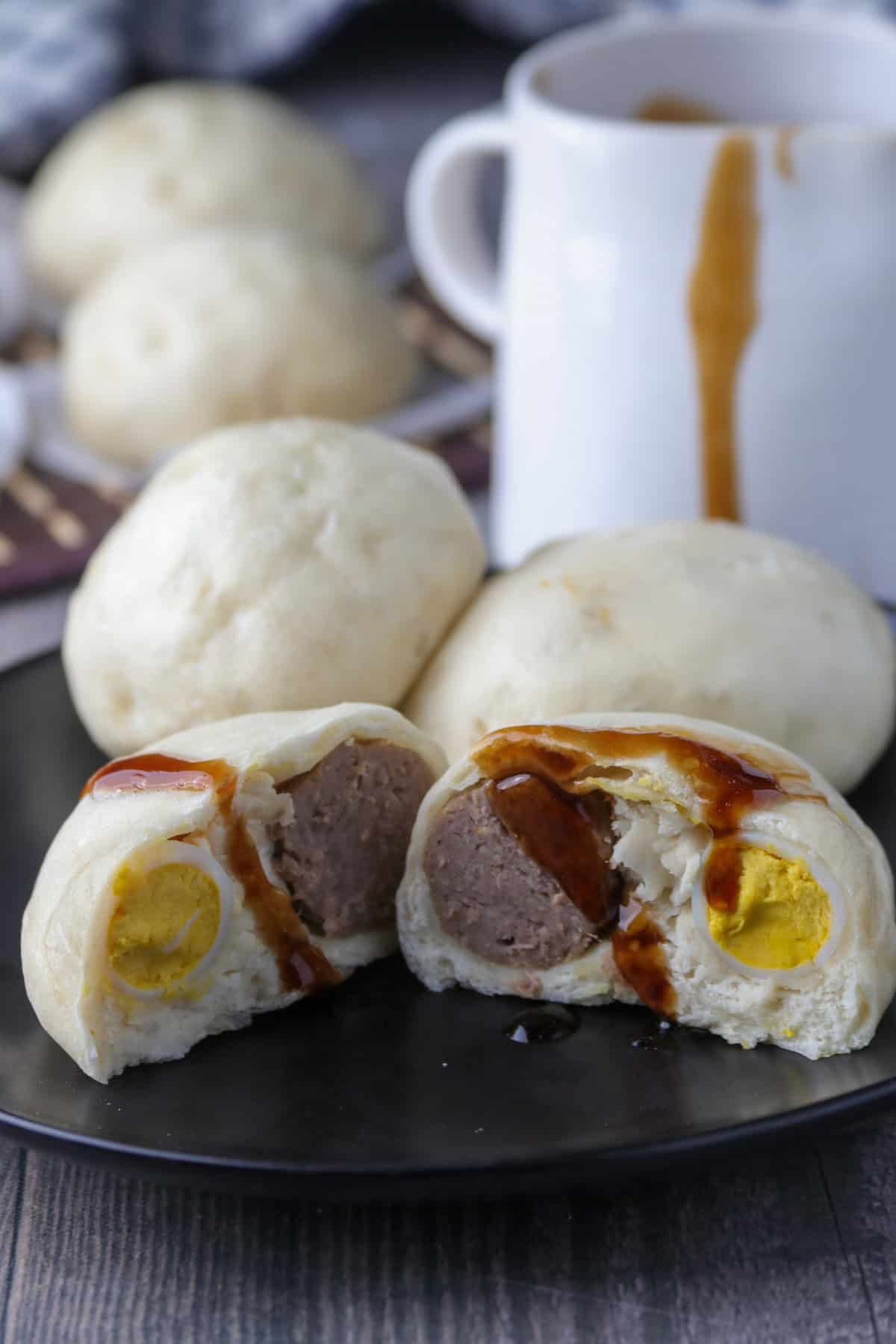 siopao buns cut in half on a black serving plate with siopao sauce on the side.