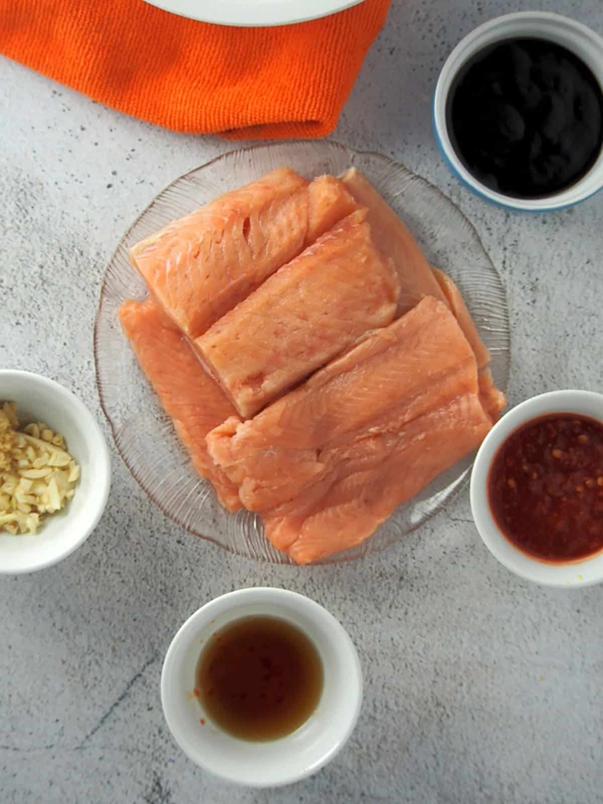 raw salmon fillets on a clear platter with hoisin marinade ingredients on the side
