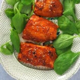 Hoisin-Glazed Salmon fillets on a serving platter with fresh spinach leaves
