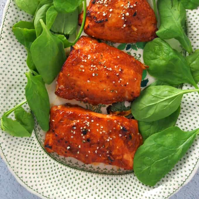Hoisin-Glazed Salmon fillets on a serving platter with fresh spinach leaves