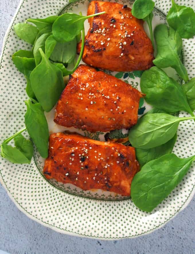 Hoisin-Glazed Salmon fillets on a serving platter with fresh spinach leaves
