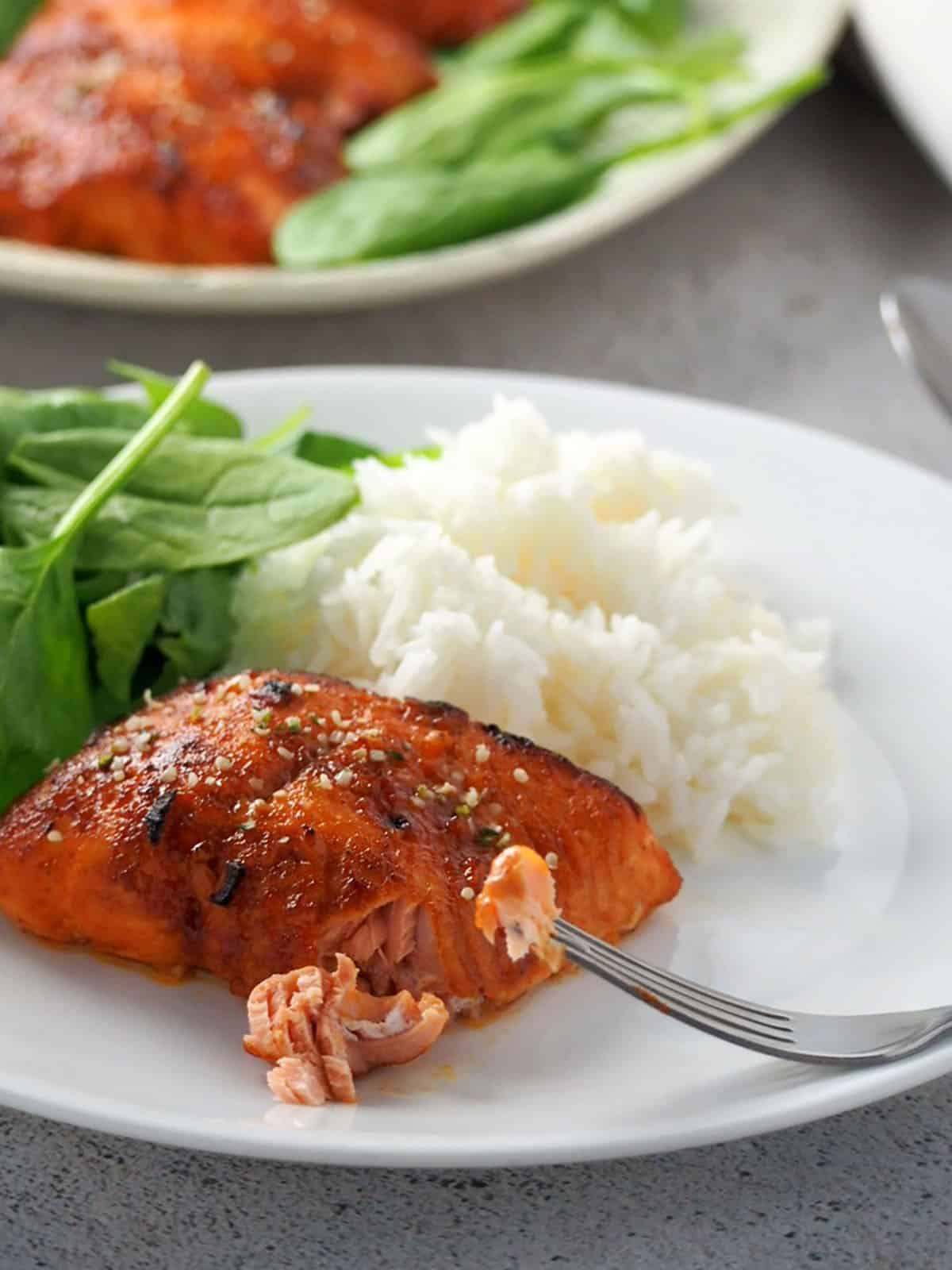 broiled salmon with hoisin glaze on a white plate with a side of steamed rice and fresh spinach