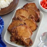 Toyomansi Pork Chops on a white platter with steamed rice, chopped tomatoes, and salted eggs on the side