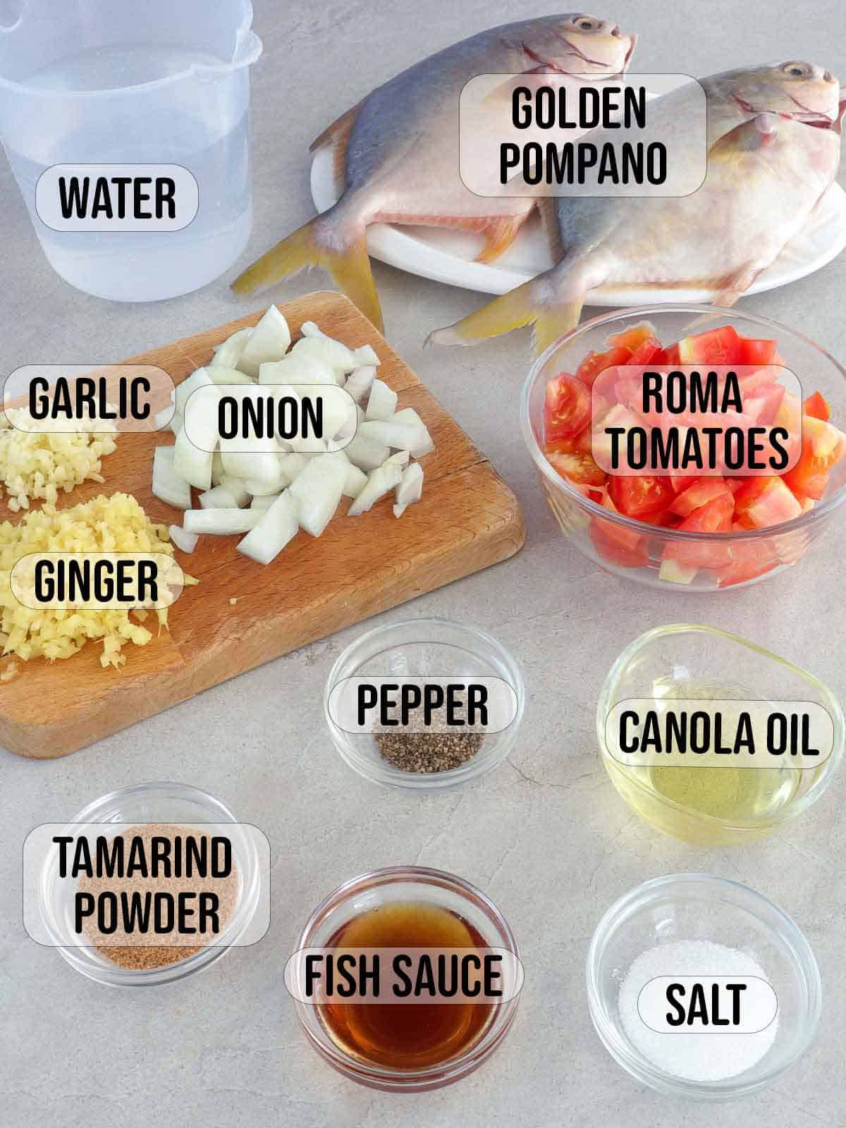 golden pompano, fish sauce, tamarind powder, tomatoes, ginger, garlic, onions, oil, water, salt, pepper in bowls.