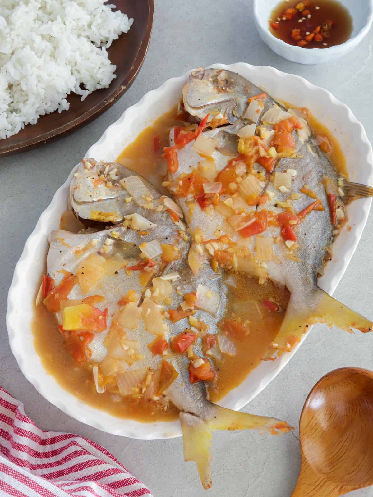 Pinangat na isda on a white serving platter with a side of steamed rice in a white platter with a plate of steamed rice in the background.