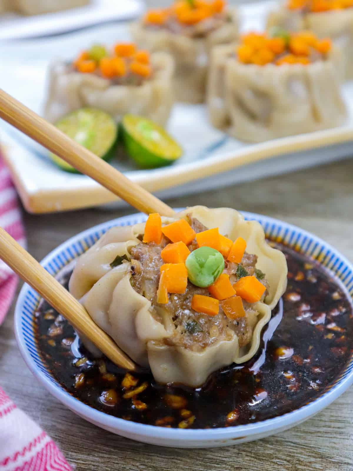 dipping pork shumai in dipping sauce using chopsticks.