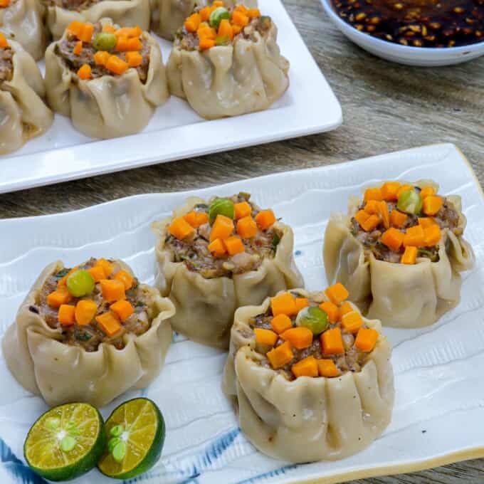 pork siomai on a white plate with calamansi and soy sauce on the side.