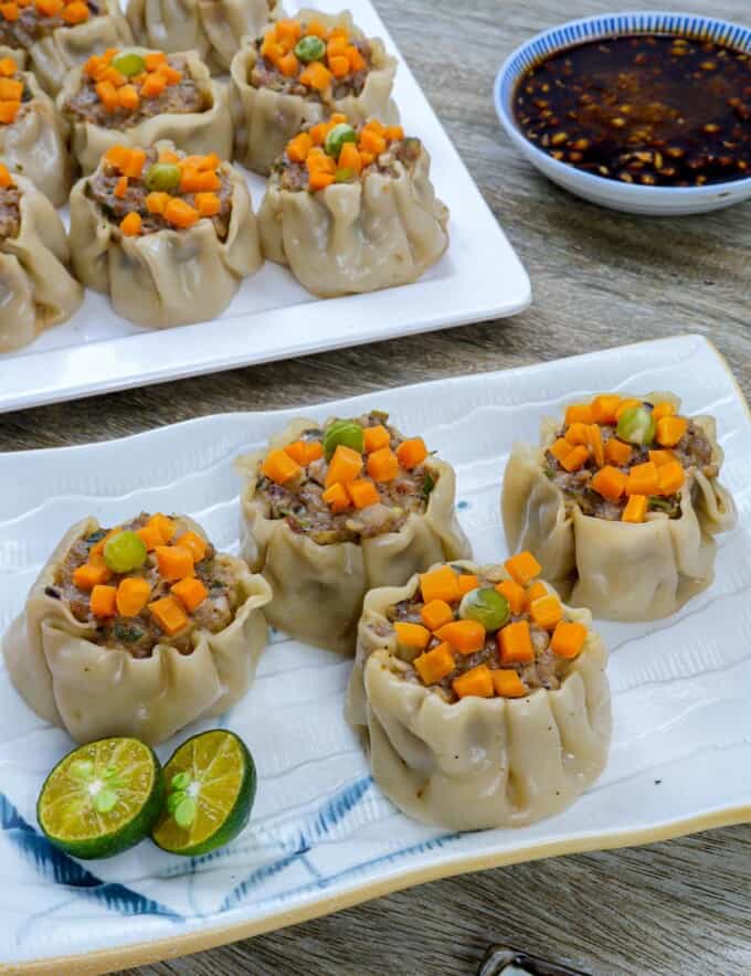 pork siomai on a white plate with calamansi and soy sauce on the side.