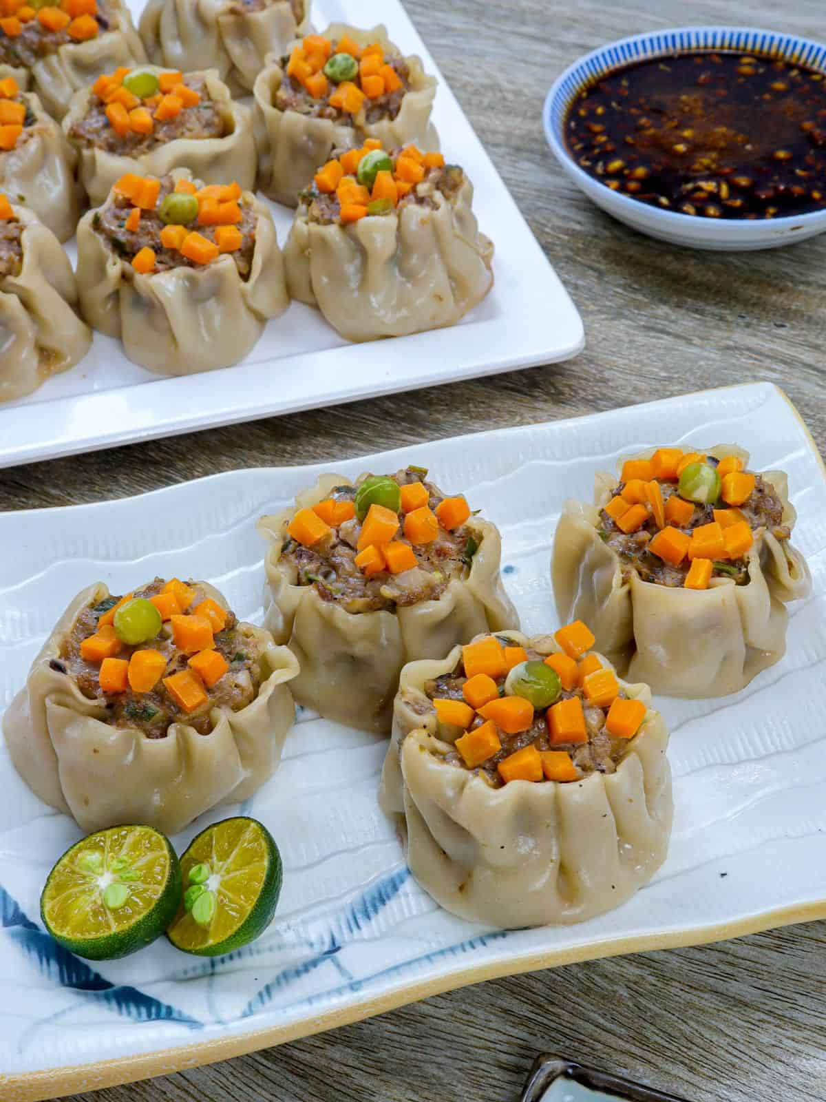 pork siomai on a white plate with calamansi and soy sauce on the side.