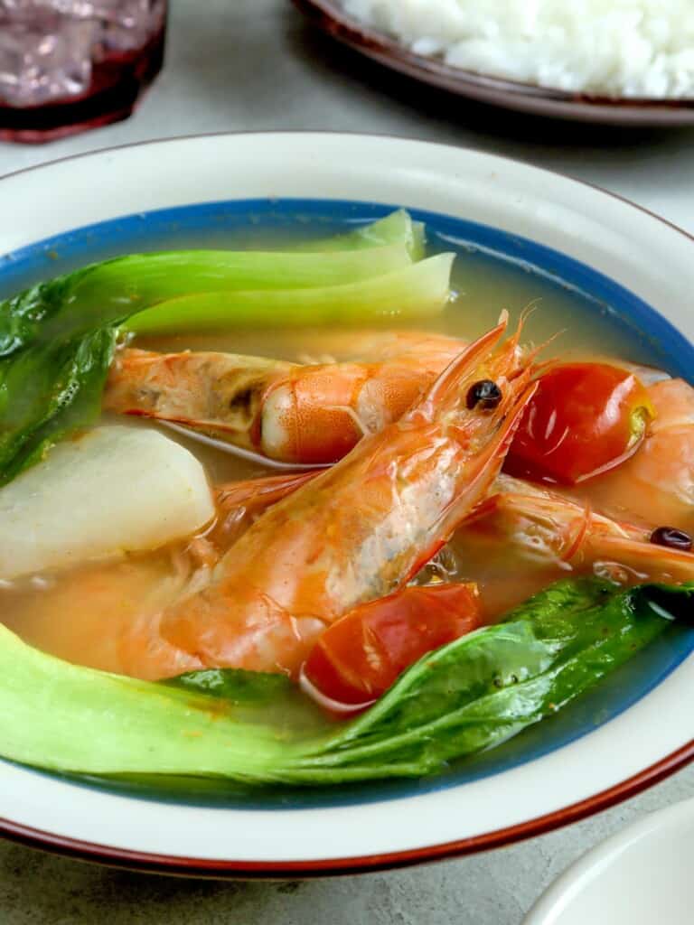 sinigang na hipon with pak choi, radish, and calamansi in a white serving bowl with a side of steamed rice
