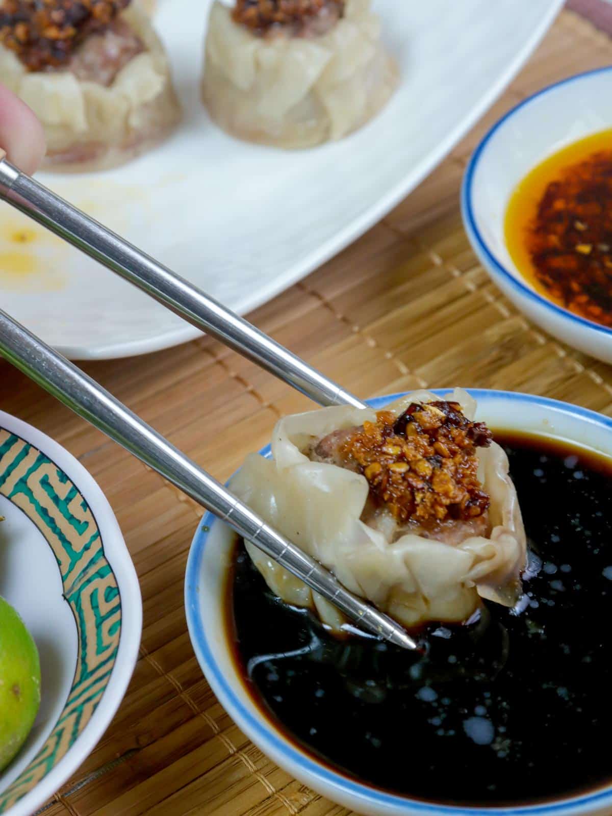 dipping pork shumai in dipping sauce using chopsticks