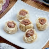 pork siomai on a white plate with calamansi and soy sauce on the side